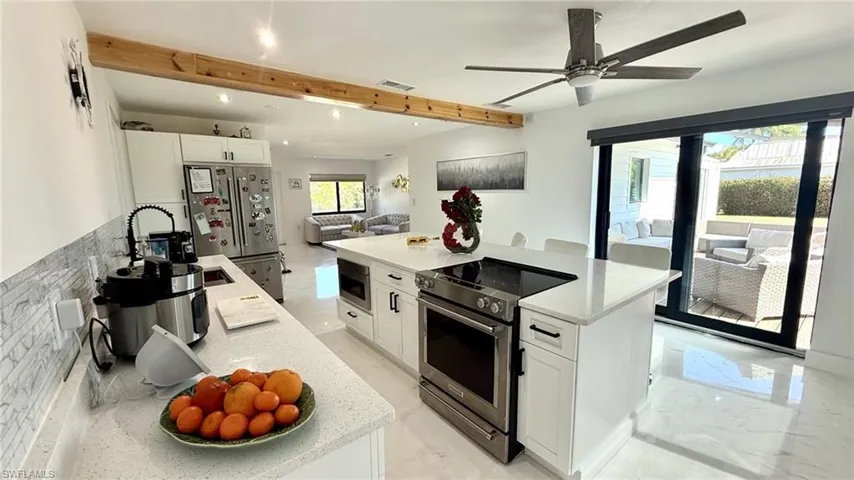 Kitchen with white cabinets, stainless steel appliances, a center island, open floor plan, and light stone countertops