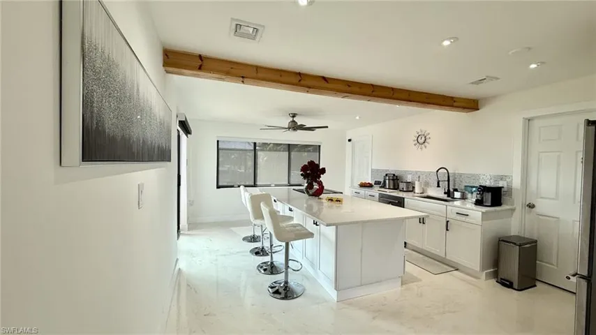 Kitchen featuring a kitchen island, a breakfast bar area, beam ceiling, tasteful backsplash, and stainless steel refrigerator