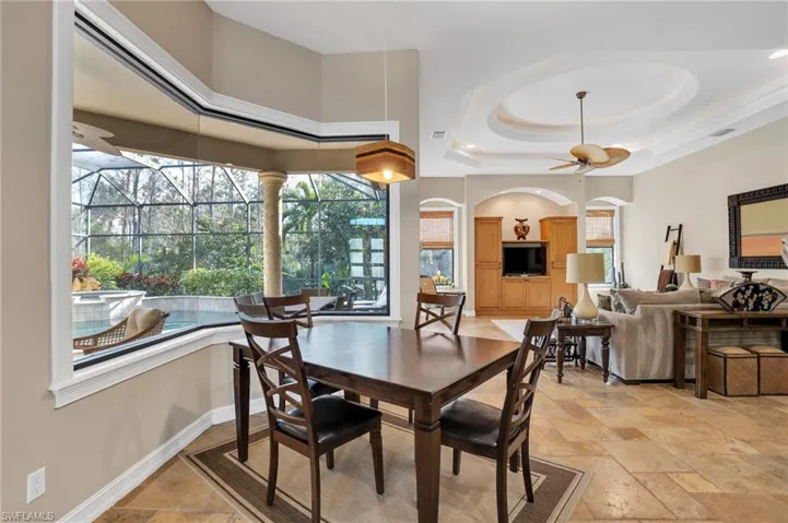 Dining area with a sunroom, a ceiling fan, stone tile flooring, and a raised ceiling