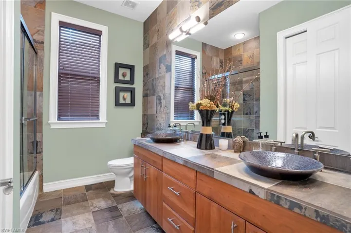 Full bathroom featuring double vanity, shower / bath combination with glass door, and stone finish floors