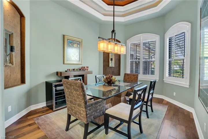 Dining room with ornamental molding, dark wood-style floors, a raised ceiling, and beverage cooler