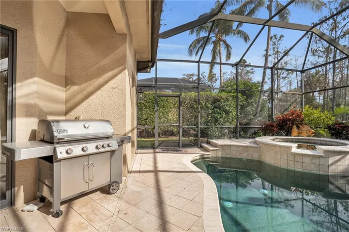 Combined pool / hot tub with a patio area, a sunroom, glass enclosure, and grilling area