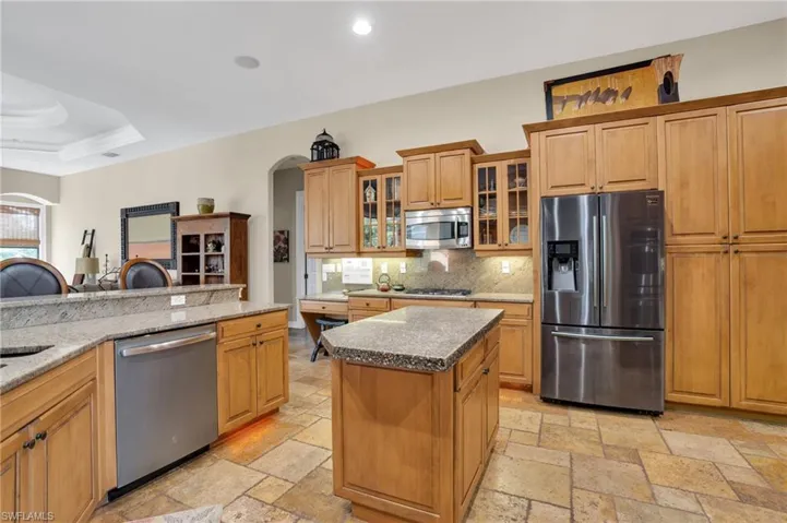 Kitchen featuring stainless steel appliances, light stone countertops, glass insert cabinets, and wood finish cabinetry