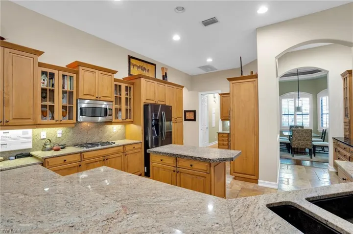 Kitchen featuring glass insert cabinets, stainless steel appliances, arched walkways, decorative backsplash, and stone tile flooring