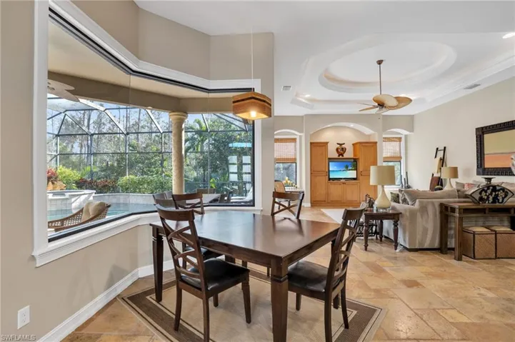 Dining area with a sunroom, ceiling fan, stone tile floors, and a tray ceiling