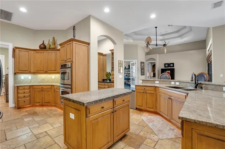Kitchen featuring arched walkways, a center island, dark stone countertops, stainless steel double oven, and a tray ceiling