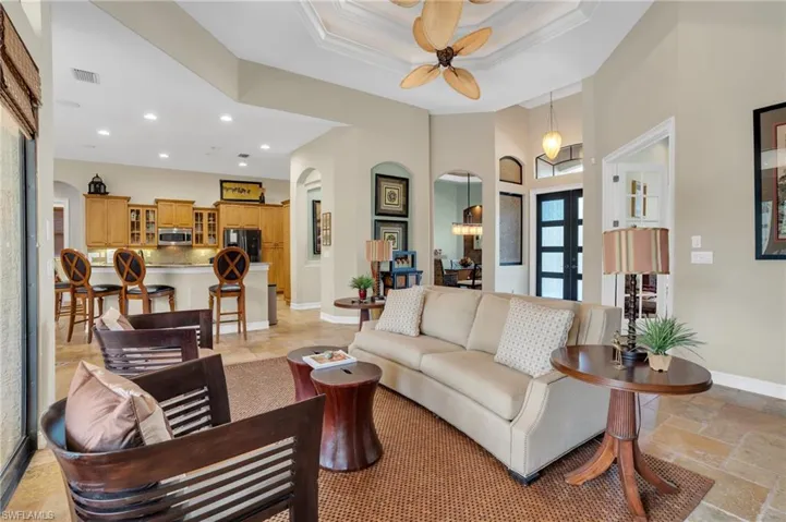 Living room with arched walkways, stone tile floors, a ceiling fan, recessed lighting, and a tray ceiling