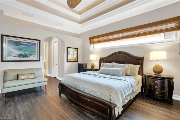 Bedroom featuring dark wood-style flooring, crown molding, arched walkways, and a raised ceiling