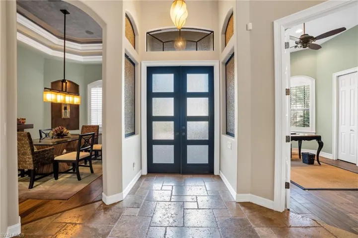 Foyer with stone tile floors, a ceiling fan, french doors, ornamental molding, and a high tray ceiling
