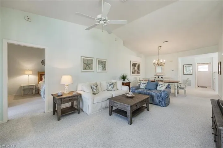 Living room featuring baseboards, light colored carpet, ceiling fan with notable chandelier, and high vaulted ceiling