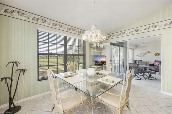 Dining space featuring light tile patterned floors, baseboards, lofted ceiling, an inviting chandelier, and wallpapered walls