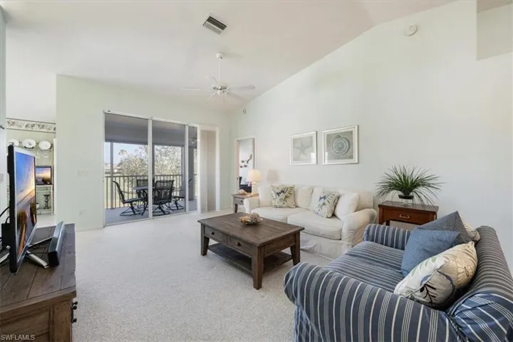 Carpeted living area featuring a ceiling fan, baseboards, vaulted ceiling, and visible vents