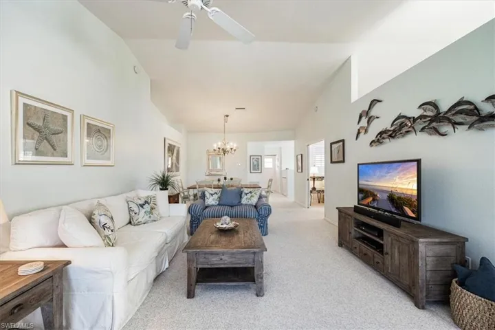 Living room featuring vaulted ceiling, ceiling fan with notable chandelier, and light colored carpet