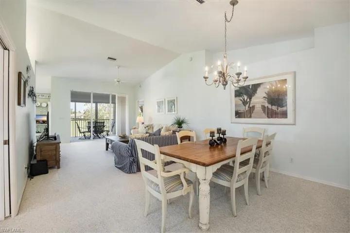 Carpeted dining room featuring visible vents, ceiling fan with notable chandelier, and lofted ceiling