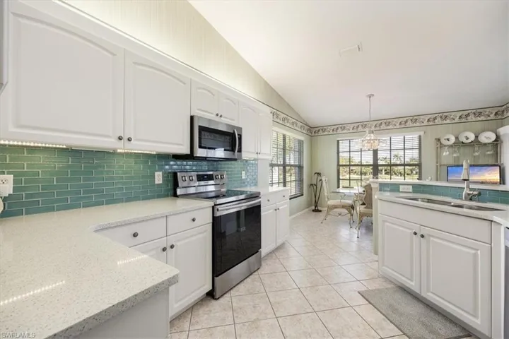 Kitchen with a notable chandelier, appliances with stainless steel finishes, a sink, decorative backsplash, and vaulted ceiling