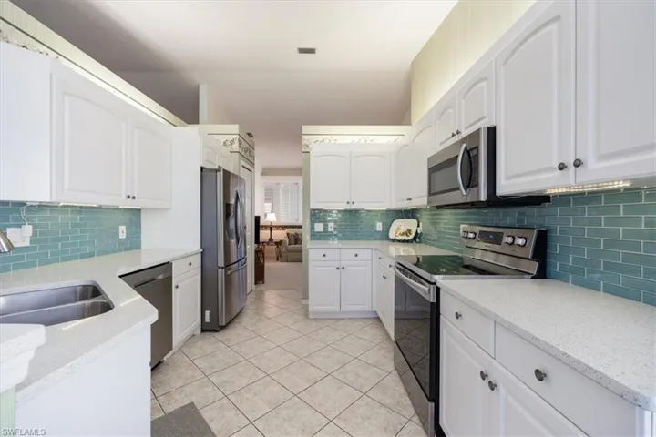 Kitchen with tasteful backsplash, a sink, light tile patterned floors, stainless steel appliances, and white cabinetry