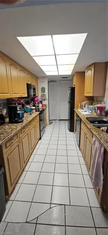 Kitchen with stove, refrigerator, light stone countertops, dishwashing machine, and light tile patterned flooring