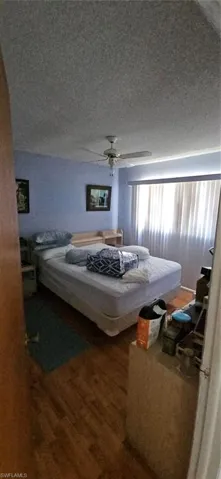 Bedroom featuring vaulted ceiling, ceiling fan, hardwood / wood-style floors, and a textured ceiling