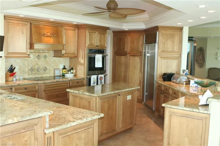 Kitchen featuring ornamental molding, a tray ceiling, appliances with stainless steel finishes, decorative backsplash, and premium range hood, Built in Sub-Zero refrigerator and brand new Monogram wall mounted double ovens