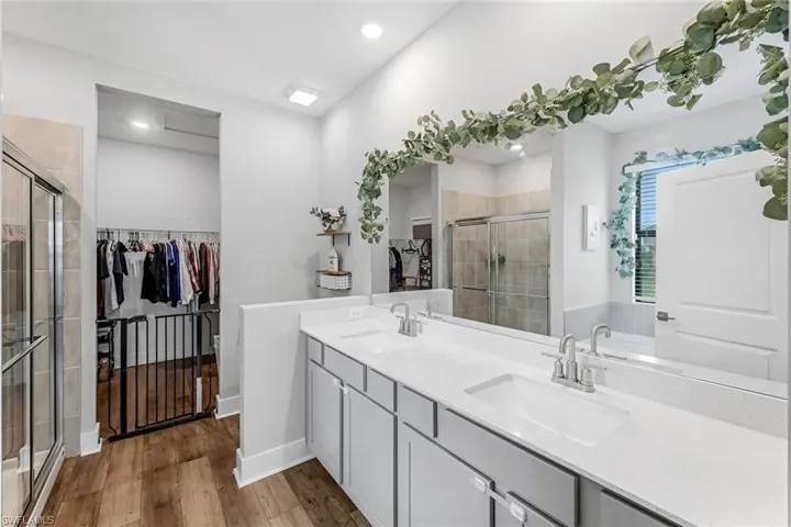 Bathroom featuring wood finished floors, a spacious closet, a sink, and a stall shower