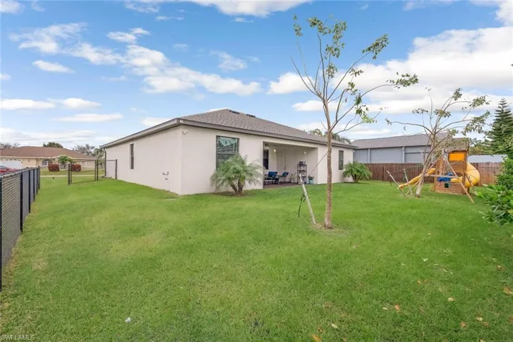 Rear view of house with a fenced backyard, a playground, a yard, a patio, and stucco siding