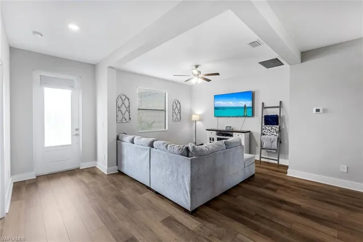 Living room featuring dark wood-style floors, a ceiling fan, visible vents, and plenty of natural light