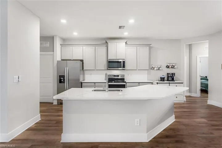 Kitchen with baseboards, a center island with sink, a sink, dark wood finished floors, and appliances with stainless steel finishes