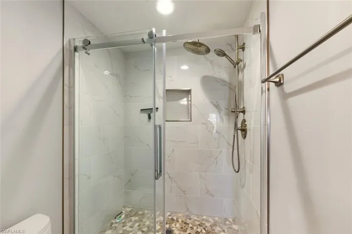 Full bathroom with a marble finish shower and toilet
