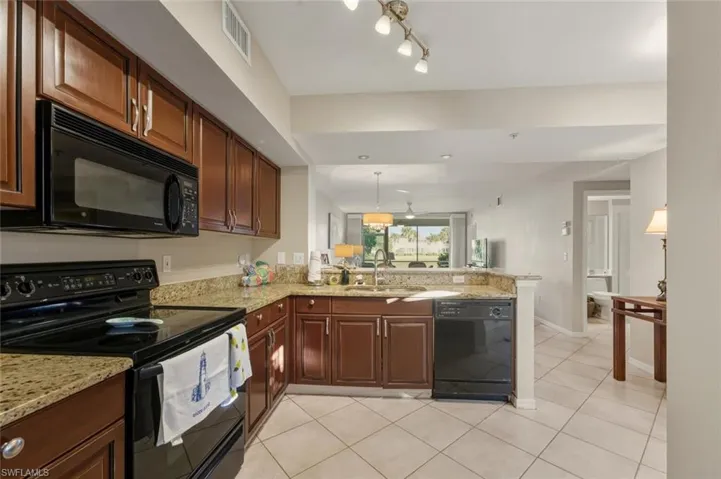 Kitchen with black appliances, a peninsula, pendant lighting, light tile patterned flooring, and light stone counters