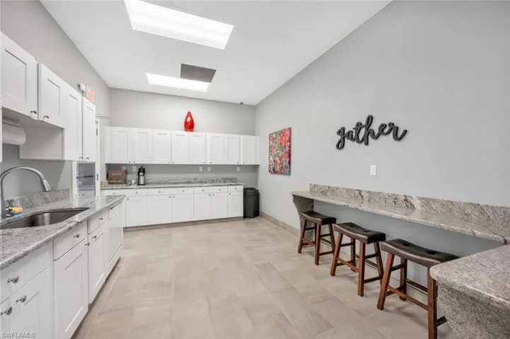 Kitchen featuring white cabinetry, light stone countertops, a kitchen bar, and dishwasher