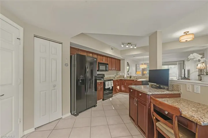 Kitchen with black appliances, light tile patterned floors, light stone counters, a peninsula, and hanging light fixtures