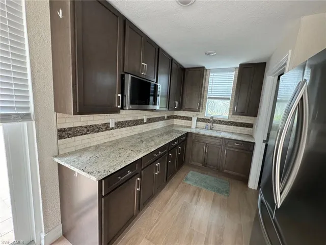Kitchen featuring light stone counters, sink, tasteful backsplash, appliances with stainless steel finishes, and light wood-type flooring