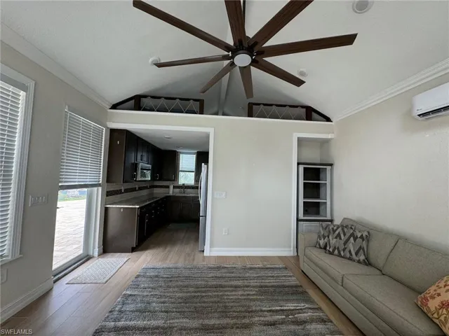 Unfurnished living room featuring light wood-type flooring, a wall unit AC, lofted ceiling, crown molding, and ceiling fan