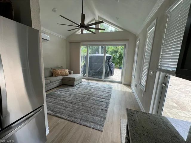 Living room featuring light wood-type flooring, crown molding, vaulted ceiling with beams, a wall mounted air conditioner, and ceiling fan