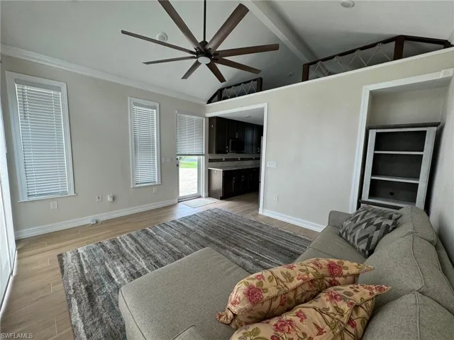 Living room featuring vaulted ceiling with beams, crown molding, ceiling fan, and hardwood / wood-style flooring
