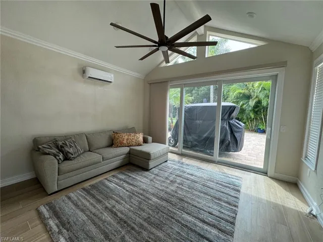Living room featuring a wall unit AC, vaulted ceiling, light hardwood / wood-style flooring, crown molding, and ceiling fan