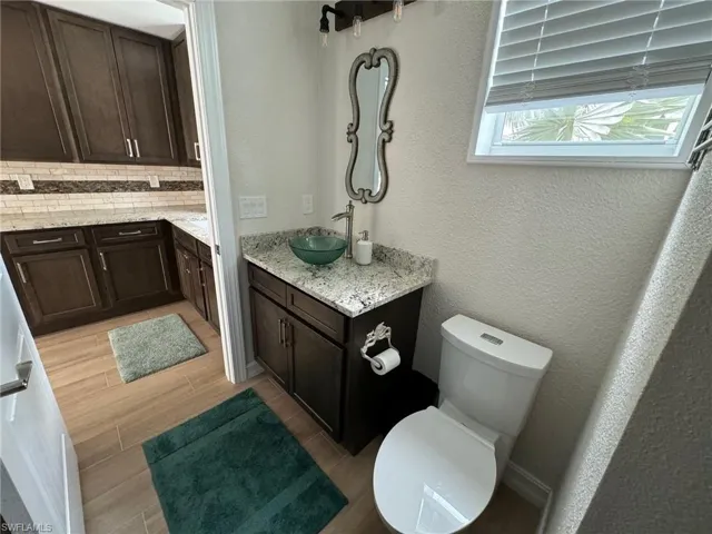 Bathroom featuring wood-type flooring, decorative backsplash, vanity, and toilet