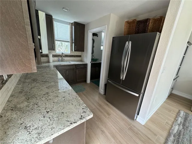 Kitchen with sink, dark brown cabinets, stainless steel refrigerator, light stone countertops, and light hardwood / wood-style floors