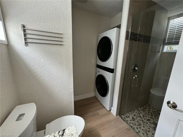 Laundry room with light hardwood / wood-style flooring, stacked washer and dryer, and a textured ceiling