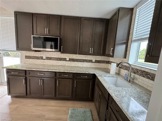 Kitchen with dark brown cabinets, backsplash, sink, and light stone countertops