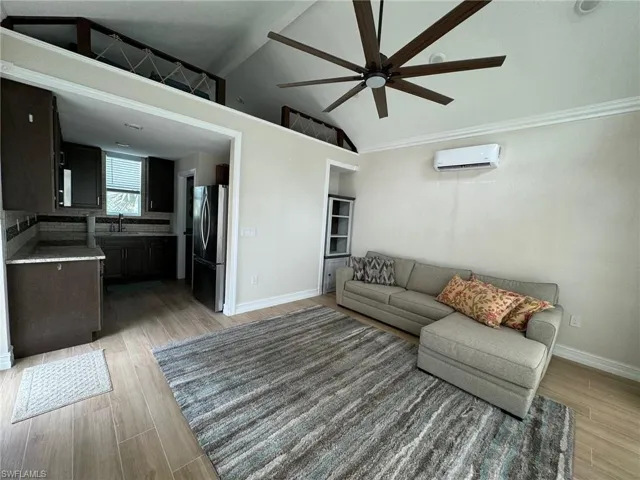 Living room featuring light hardwood / wood-style floors, lofted ceiling, ceiling fan, a wall unit AC, and sink