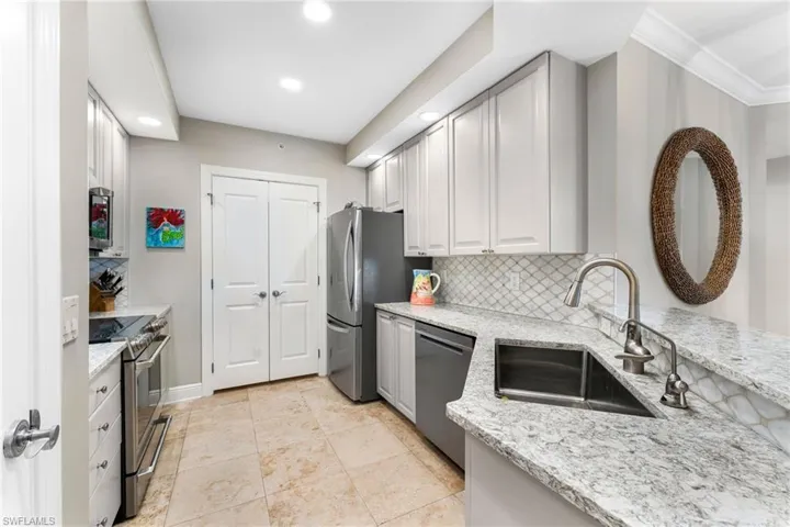 Kitchen featuring light stone countertops, backsplash, stainless steel appliances, and sink