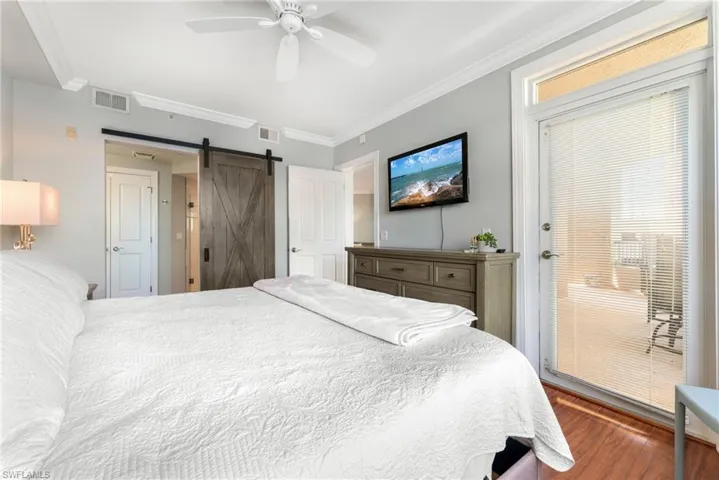 Bedroom featuring a barn door, ceiling fan, crown molding, and dark hardwood / wood-style floors