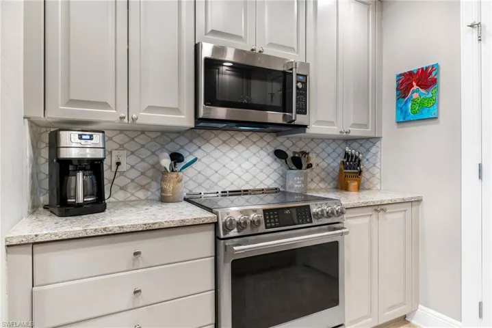 Kitchen featuring tasteful backsplash, light stone counters, and appliances with stainless steel finishes