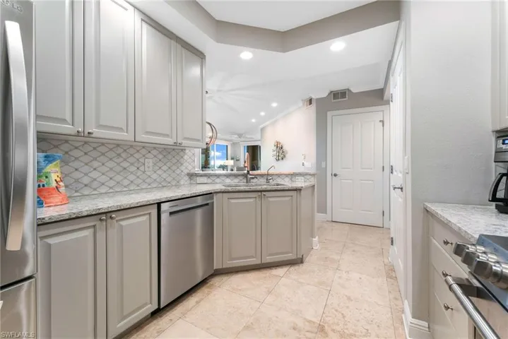 Kitchen featuring gray cabinetry, sink, decorative backsplash, light stone countertops, and stainless steel appliances
