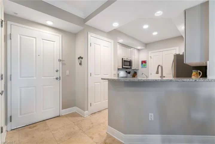 Kitchen with backsplash, white cabinets, ornamental molding, appliances with stainless steel finishes, and kitchen peninsula