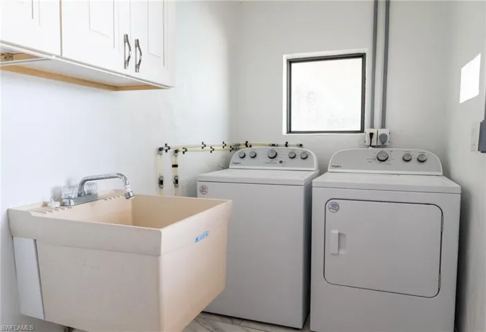 Laundry area featuring cabinet space, marble finish floor, washer and dryer, and a sink