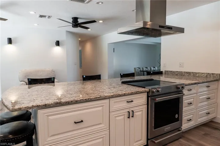 Kitchen with a ceiling fan, stainless steel stove, light stone counters, wall chimney exhaust hood, and visible vents
