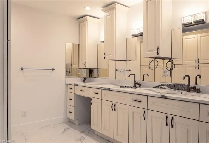 Full bathroom featuring double vanity, marble finish floor, baseboards, and a sink