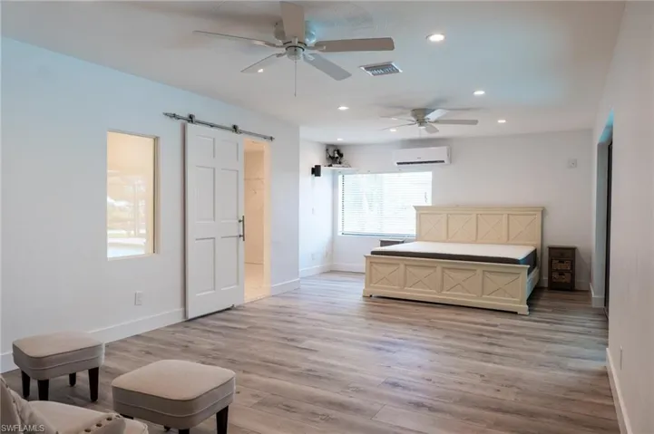 Bedroom with a barn door, recessed lighting, visible vents, a wall unit AC, and baseboards